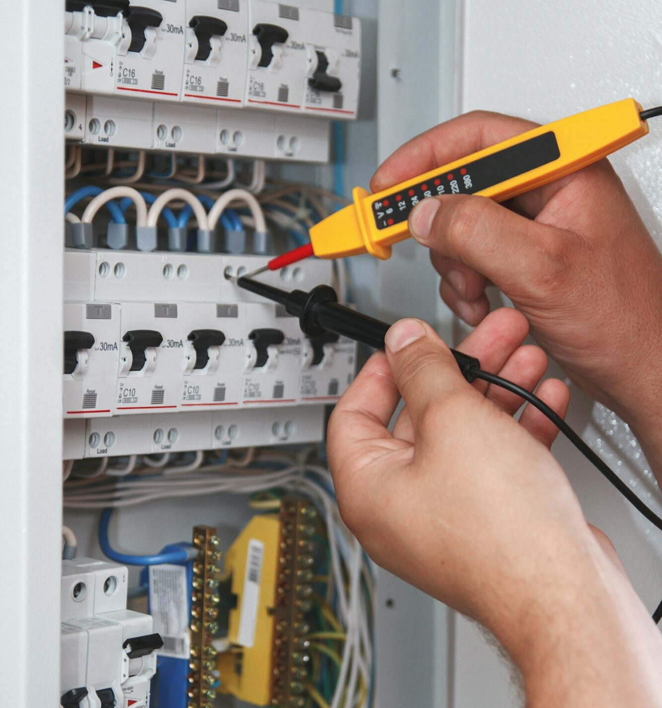 Electrician with multimeter probe at an electrical switchgear ca