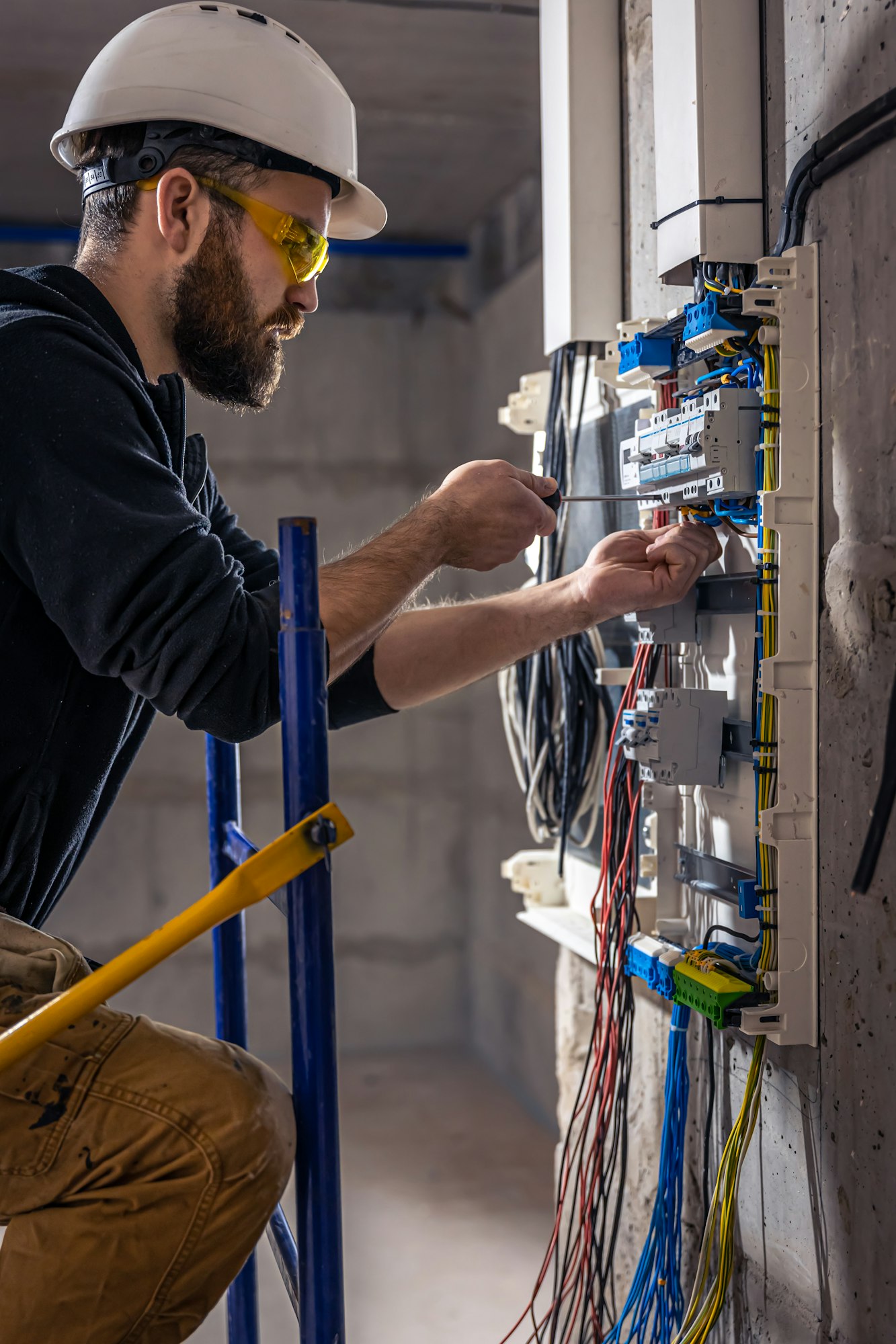 A male electrician works in a switchboard with an electrical connecting cable.