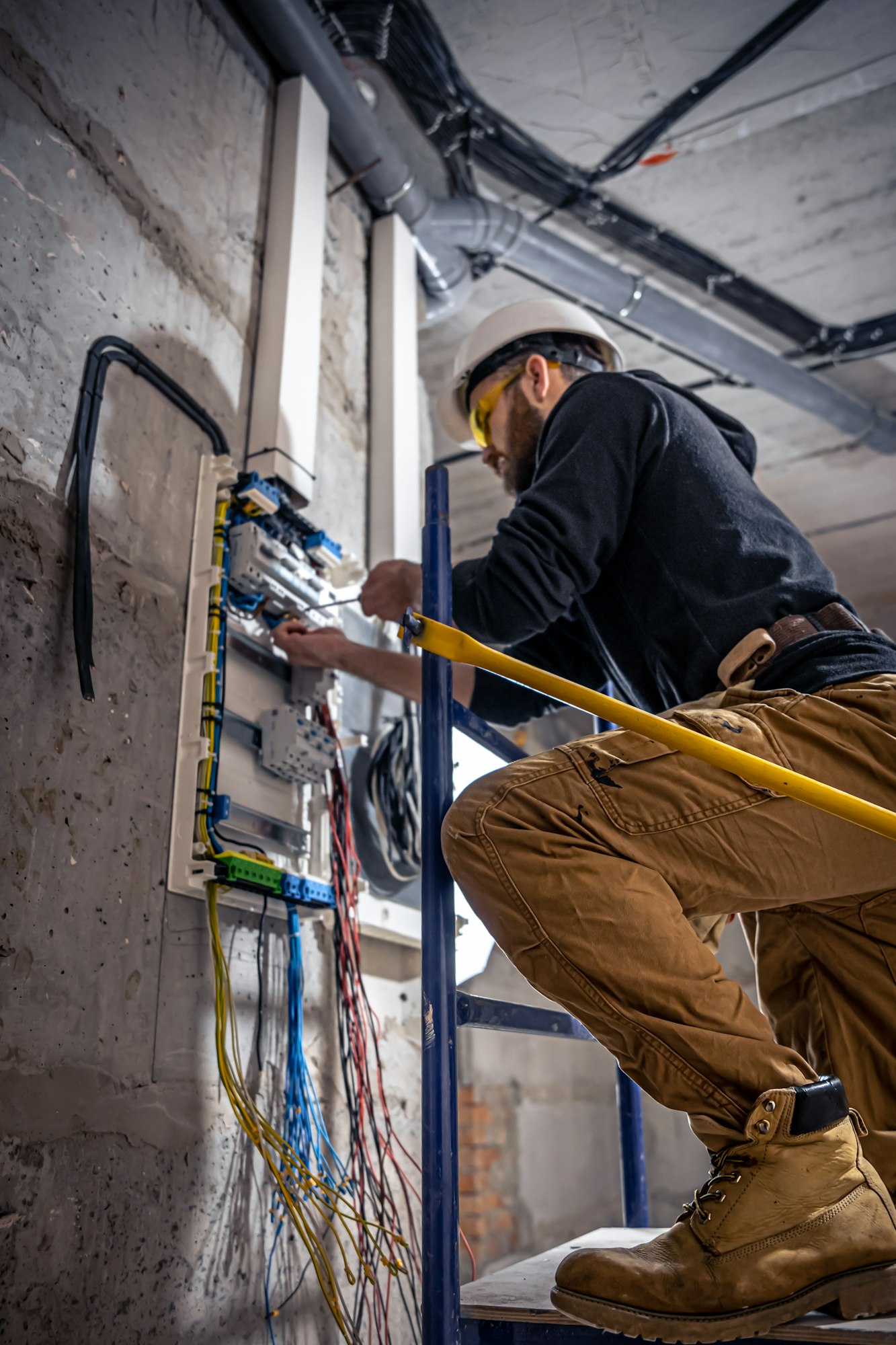 A male electrician works in a switchboard with an electrical connecting cable.